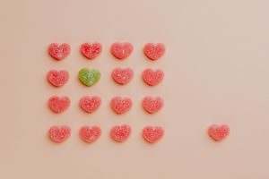 heart shaped gummy candy assorted in rows with one candy aside against pink background